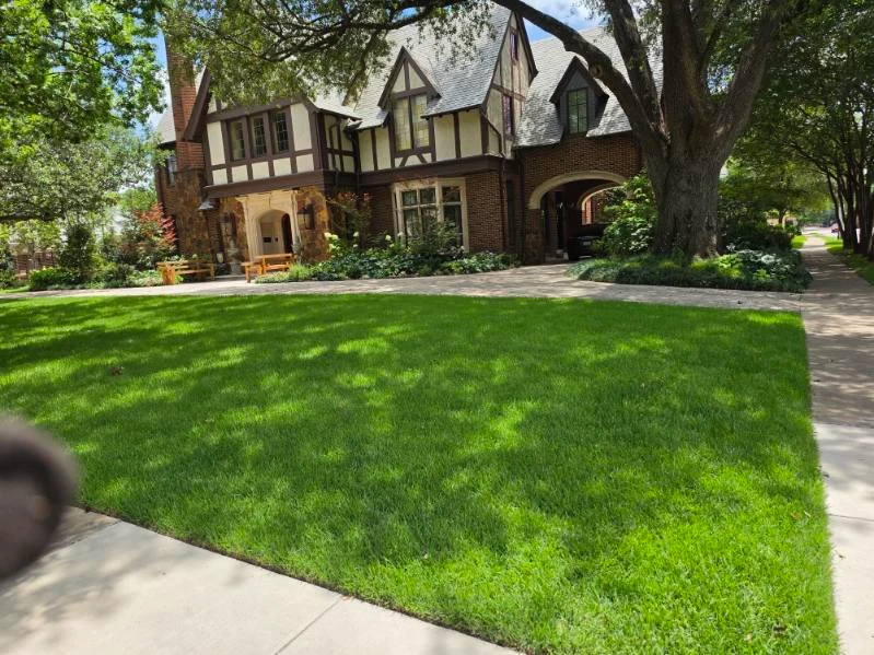 A broad lawn is framed by mature trees and layered planting around the home.